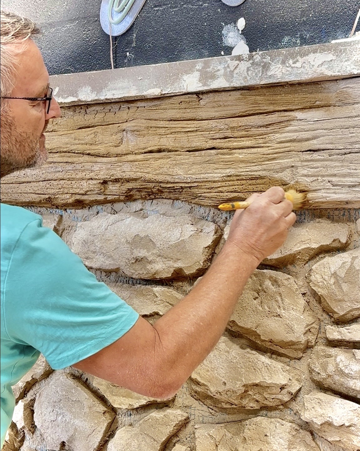 Thierry BKLK applique la patine sur un décor Bois de Bonnieux sculpté au-dessus d’un mur en pierre