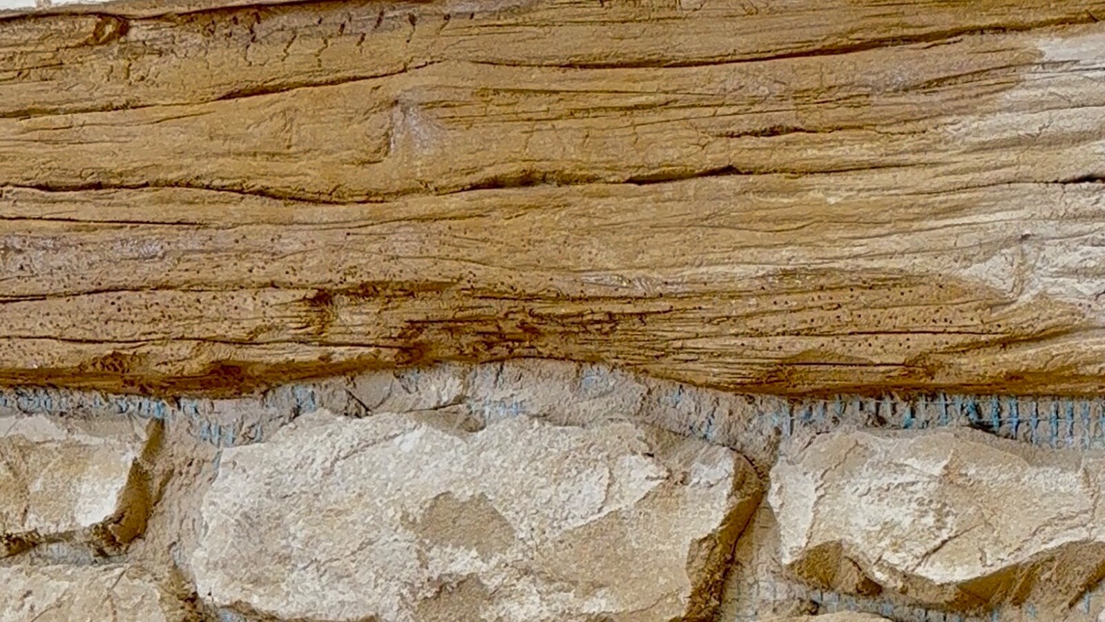 Détail du décor Bois de Bonnieux, effet bois sculpté et patiné à la main au-dessus d’un mur en pierre